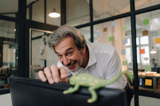 Happy senior businessman with chameleon figurine in office