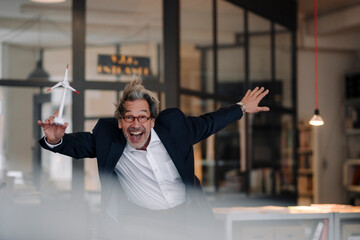 Excited senior businessman with wind turbine model in office