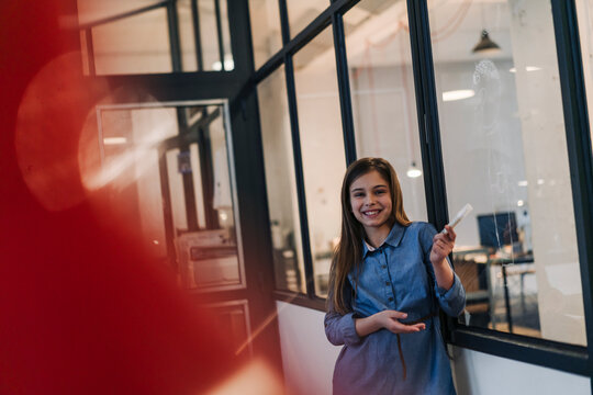 Happy girl drawing on glass pane in office
