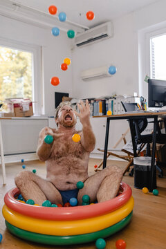 Crazy businessman sitting in wading pool in office playing with balls