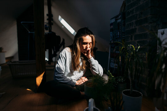 Serious young woman sitting on attic with plants