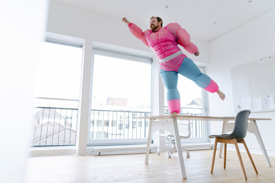 Businessman in office wearing pink bodybuilder costume pretending to fly