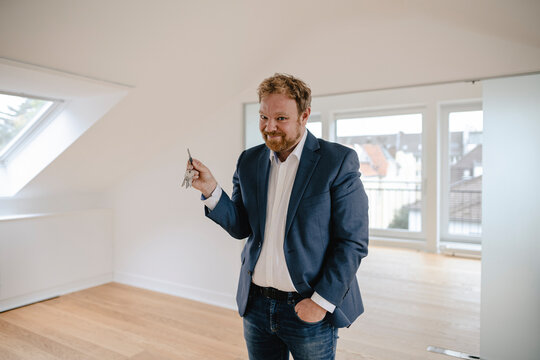 Portrait of smiling businessman standing in empty apartement holding key