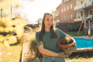Portrait of young woman in garden holding seedling in flowerpot