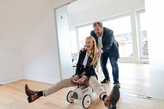 Playful businessman pushing businesswoman on toy car in office