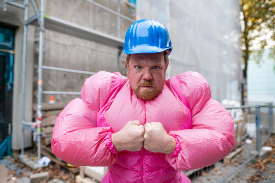 Portrait of man wearing pink bodybuilder costume and hard hat at construction site