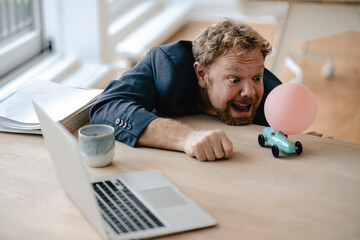 Businessman playing with miniature toy car on desk in office