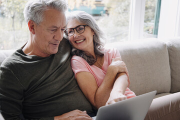 Happy senior couple with laptop relaxing on couch at home