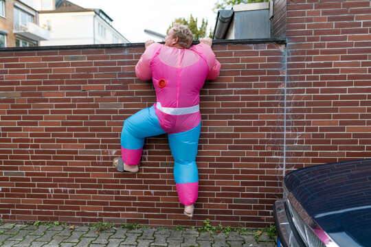 Man wearing pink bodybuilder costume climbing over a wall