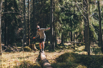 Young man balancing on tree trunk, looking through VR glasses