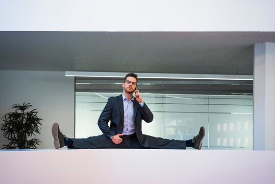 Businessman doing the splits on reception desk in office talking on cell phone