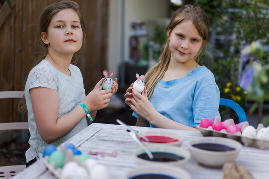 Portrait of two girls decorating Easter eggs on garden table