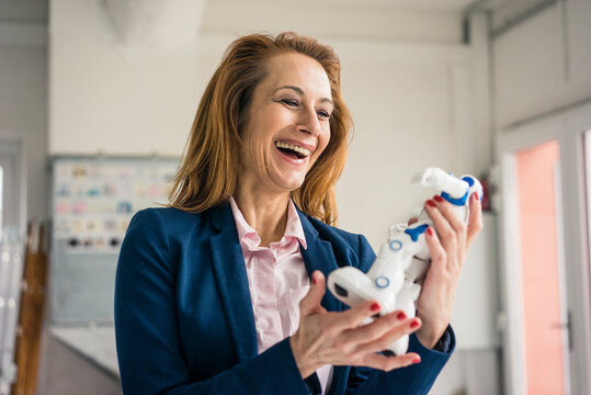 Mature businesswoman holding toy robot, laughing
