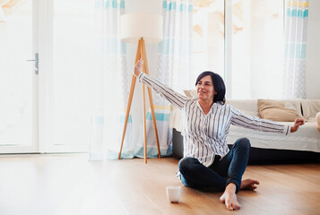 Mature woman sitting on floor at home, relaxing with a cup of coffee