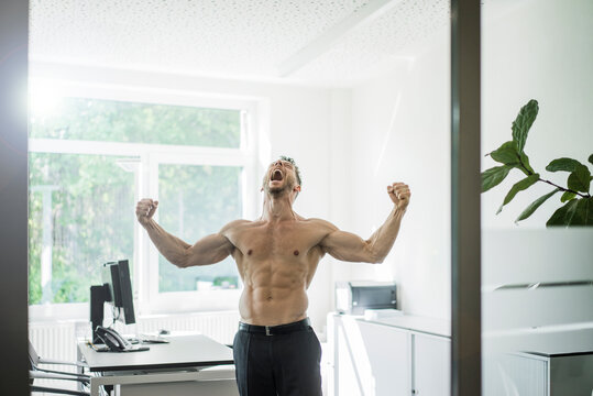 Screaming barechested businessman flexing muscles in office