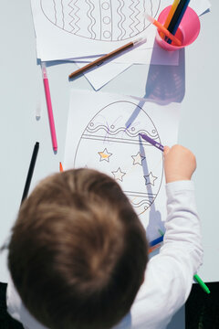 Top view of toddler coloring Easter egg on a paper
