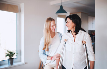 Daughter helping her mother to walk with crutches
