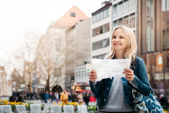 Portrait of smiling blond woman with map and baggage in the city, Munich, Germany