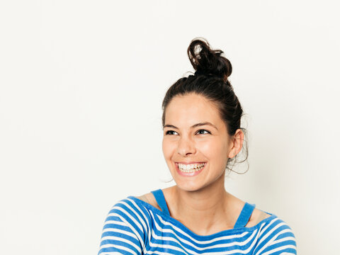 Beautiful young woman with black hair and blue white striped sweater is posing in front of white background