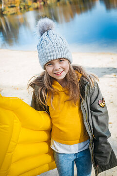 Portrait of smiling girl with yellow airbed at lakeshore in autumn