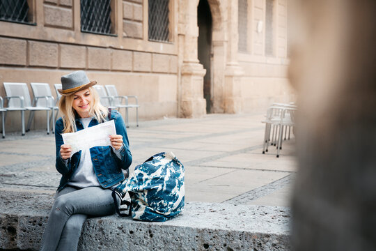Smiling blond woman with baggage sitting on curb looking at map