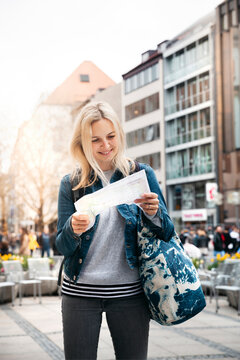 Portrait of smiling blond woman baggage looking at map in the city, Munich, Germany