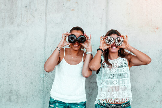 Two friends standing side by side looking through doughnuts