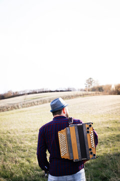Back view of man with accordion on his shoulder on a meadow