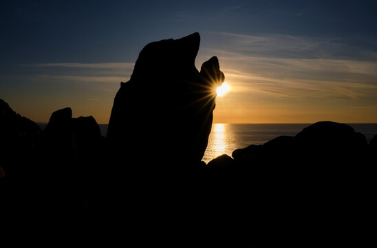 Italy, Province of Sassari, Santa Teresa Gallura, Sun setting behind silhouette of Cape Testa boulder