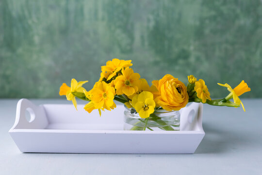 Persian buttercup, daffodil, primrose and horned violet in glass on wooden tray