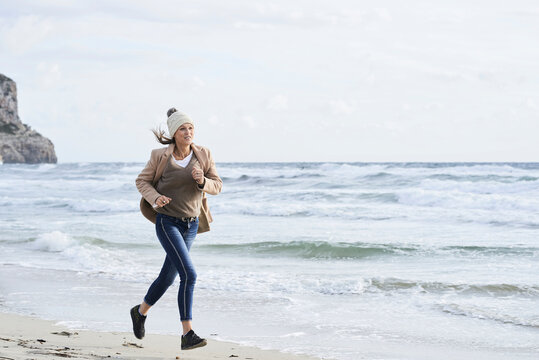 Spain, Menorca, senior woman jogging on the beach in winter - Powered by Adobe