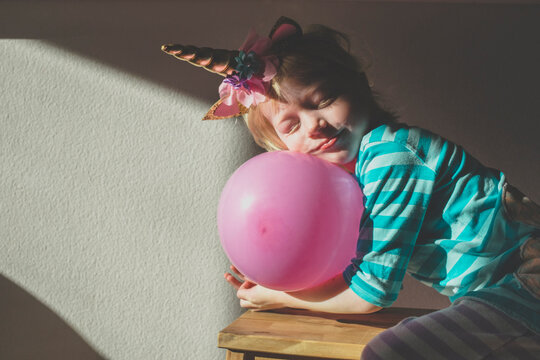 Portrait of little girl with eyes closed wearing unicorn horn leaning on pink balloon