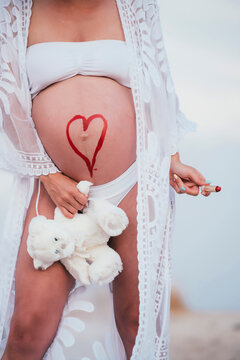 Pregnant woman with a drawn heart on her belly holding a teddy bear