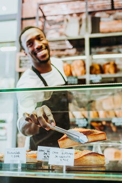 Smiling man working in a bakery taking a piece of cake with a tongs