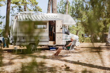 France, Gironde, woman sitting in front of camper on a camping ground using digital tablet