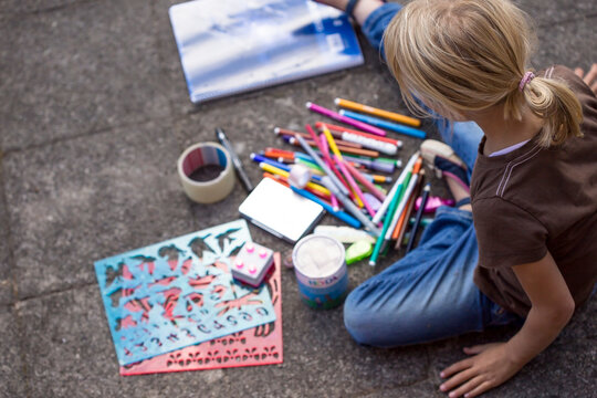 Girl sitting on pavement with many drawing materials