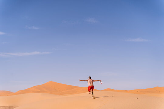 Overweight man with swimming shorts running in the desert of Morocco