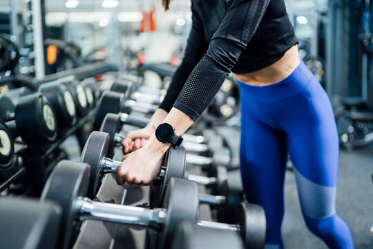 Close-up of woman taking dumbbells from rack in gym