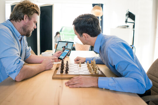 Two men playing chess and checking smartphone