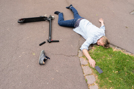 Accident Victim Lying On Road Besides E-Scooter And Smartphone