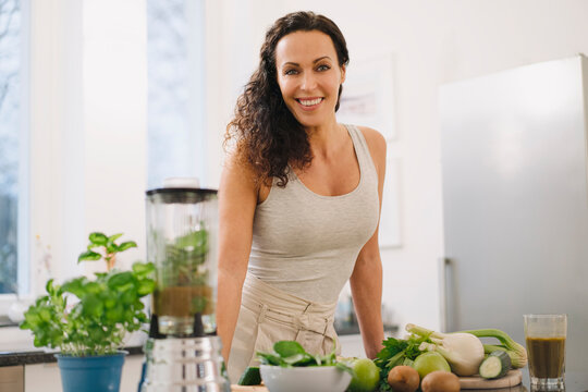 Fit woman standing in kitchen, preparing healthy smoothie