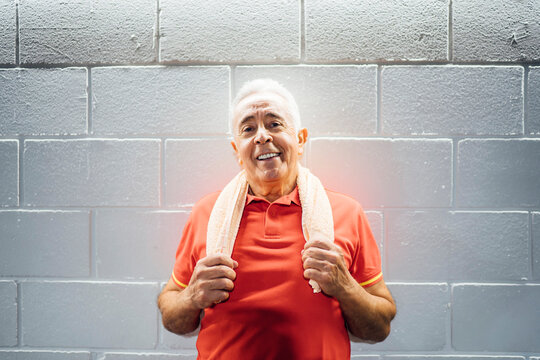 Portrait of smiling senior man having a break and leaning agianst a wall in gym