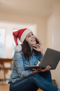 Woman with Santa hat looking for presents online, using laptop