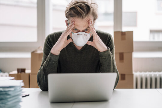 Serious businessman wearing protective mask and using laptop