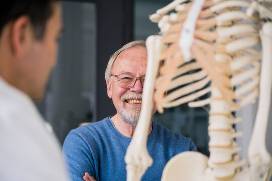 Smiling senior patient with doctor in medical practice with anatomic model