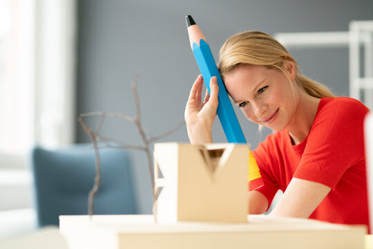 Young woman in office with oversized pen and architectural model on desk