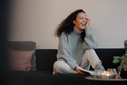 Woman sitting on couch laughing, reading a book