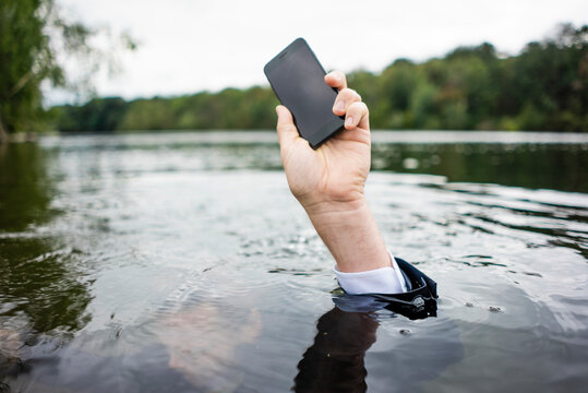 Businessman's Hand Holding Cell Phone Inside A Lake