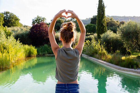 Rear view of a girl standing at swimming pool, forming a heart with her hands