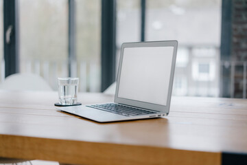 Laptop on desk in office with glass of water